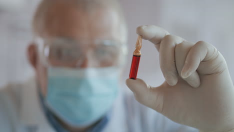 Close-up-of-the-developer-of-the-coronavirus-vaccine-holding-an-ampoule-of-red-liquid-examining-and-holding-the-vaccine-in-gloves.-High-quality-4k-footage