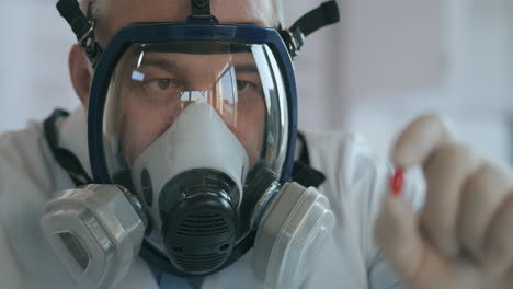 A-scientist-doctor-at-a-pharmaceutical-company-developing-a-drug-in-a-laboratory-in-a-glass-respirator-screen-holds-a-new-medicine-a-red-pill-an-antibiotic-against-the-virus-and-looks-at-it.-High-quality-4k-footage