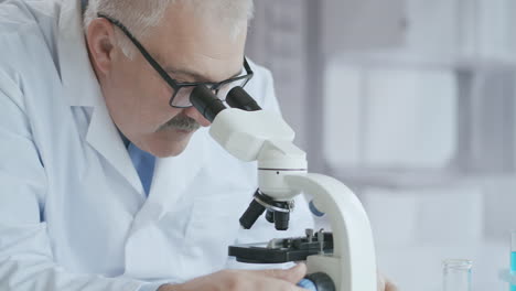 Bearded-Caucasian-male-researcher-wearing-protective-glasses-and-working-with-a-microscope-spbas.-scientist-using-microscope-in-a-laboratory.-Search-for-coronavirus-vaccine.-High-quality-4k-footage