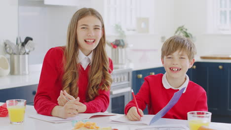 Portrait-Of-Laughing-Brother-And-Sister-Wearing-School-Uniform-Doing-Homework-On-Kitchen-Counter