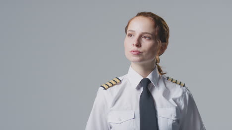 Studio-Portrait-Of-Female-Airline-Pilot-Or-Ship-Captain-Looking-Off-Camera-Against-Plain-Background
