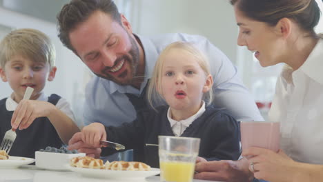 Children-Wearing-School-Uniform-In-Kitchen-Eating-Breakfast-Waffles-As-Parents-Get-Ready-For-Work