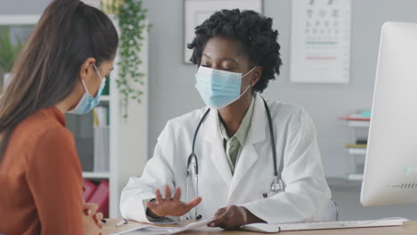 Female-Doctor-Or-Consultant-Wearing-Mask-Meeting-With-Female-Patient-To-Discuss-Scans