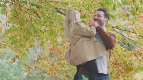 Father-Carrying-Daughter-Against-Background-Of-Autumn-Leaves-On-Countryside-Walk