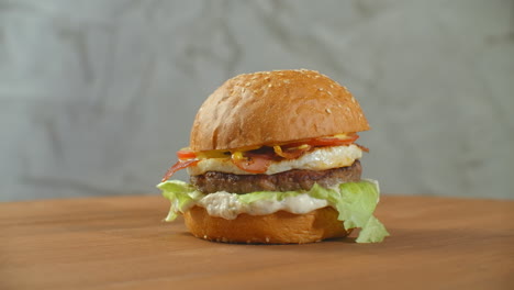 Toller-Burger-Mit-Rinderkotelett,-Tomaten,-Pilzen-Und-Gurken-Mit-Geschmolzenem-Käse-Dreht-Sich-Auf-Einem-Holzbrett-Auf-Hellem-Hintergrund.