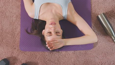 Overhead-shot-of-woman-resting-on-exercise-mat-at-home-after-workout---shot-in-slow-motion