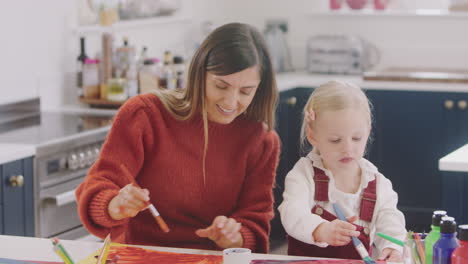 Mother-With-Daughter-At-Home-Doing-Craft-And-Painting-Picture-In-Kitchen