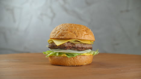 One-hamburger-on-a-board-fries-are-scattered-around.-Close-up-of-delicious-fresh-home-made-burger-with-lettuce-cheese-onion-and-tomato-on-a-rustic-wooden-plank-on-a-dark-background
