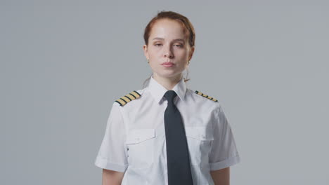 Studio-Portrait-Of-Female-Airline-Pilot-Or-Ship-Captain-Against-Plain-Background