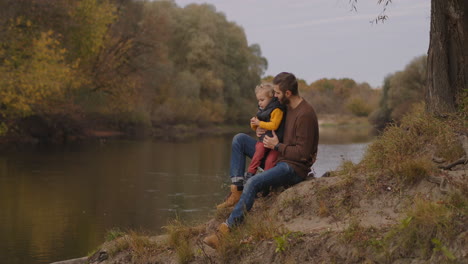 early-fall-in-forest-man-with-little-son-are-walking-at-good-weather-man-and-child-are-sitting-on-shore-of-river-family-walk-at-nature