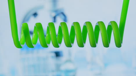 Close-up-and-slow-motion-of-green-liquid-spiraling-horizontally-from-right-to-left-in-a-scientific-glass-condenser.-development-and-search-for-a-vaccine.-Coronavirus-chemical-research.-Drug-testing.-High-quality-4k-footage