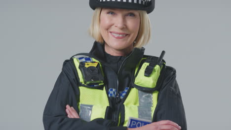 Full-Length-Studio-Portrait-Of-Smiling-Mature-Female-Police-Officer-Against-Plain-Background
