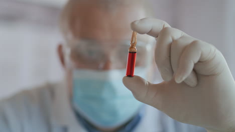 A-male-scientist-holds-a-red-glass-ampoule-with-a-vaccine-and-looks-at-it-close-up-slow-motion.-Vaccinations.-High-quality-4k-footage