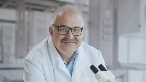 Portrait-of-a-male-doctor-in-a-laboratory-with-a-microscope-looking-at-the-camera-serious.-Doctor-the-doctor-smiles-at-the-camera.-High-quality-4k-footage