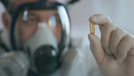 A-scientist-doctor-at-a-pharmaceutical-company-developing-a-drug-in-a-laboratory-in-a-glass-respirator-screen-holds-a-new-medicine-a-yellow-pill-an-antibiotic-against-the-virus-and-looks-at-it.-High-quality-4k-footage