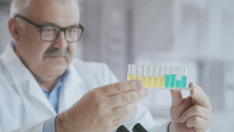 Scientist-or-technologist-doing-a-laboratory-test.-Concentrated-liquid.-male-chemist-examines-a-flask-with-a-blue-substance.-Holds-a-test-tube-in-his-hand-and-mixes-the-liquid-inside-watching-the-chemical-reaction.-High-quality-4k-footage