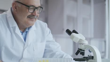 Male-Research-Scientist.-He-Sitting-in-a-High-End-Modern-Laboratory-with-Beakers-Glassware-Microscope-and-Working-Monitors-Surround-Him.-High-quality-4k-footage