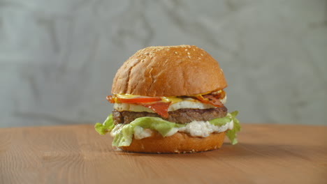 Great-Burger-with-beef-cutlet-tomatoes-mushrooms-and-cucumbers-with-melted-cheese-rotates-on-a-wooden-Board-on-light-background.