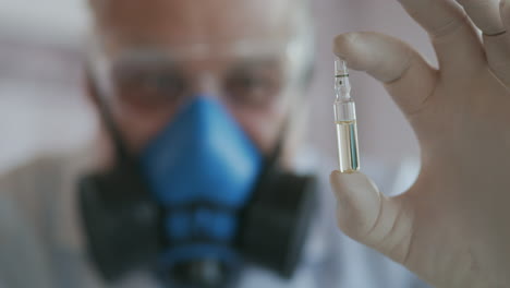 Extreme-Nahaufnahme-Eines-Wissenschaftlers-Mit-Blauem-Atemschutzgerät-Und-Schutzbrille.-Der-Entwickler-Des-Coronavirus-Impfstoffs-Hält-Eine-Weiße-Transparente-Ampulle-In-Der-Hand.-Der-Arzt-Betrachtet-Den-Neuen-Impfstoff.-Hochwertiges-4K-Filmmaterial