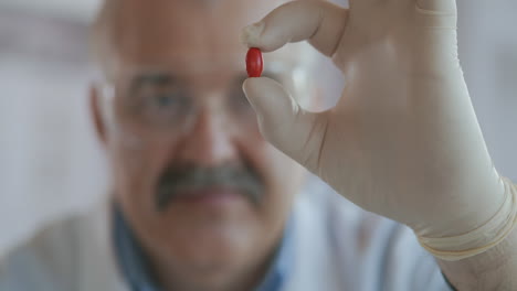 A-male-scientist-holds-a-red-pill-in-his-hands-and-looks-at-it-close-up-slow-motion.-High-quality-4k-footage