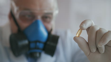 Extreme-Close-up-of-a-scientist-in-a-blue-respirator-and-protective-glasses-who-developed-a-coronavirus-vaccine-holding-a-white-pill.-The-doctor-looks-at-the-painkillers-antiviral-medication.-Vitamins.-High-quality-4k-footage