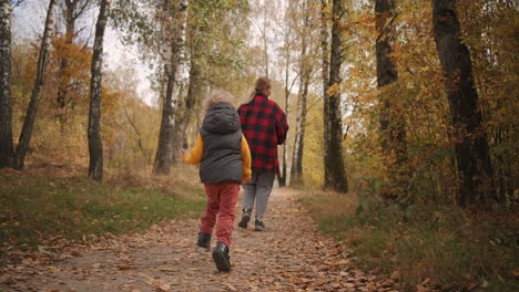 young-woman-and-little-child-are-running-in-autumn-forest-over-walkpath-son-is-following-mother-catch-up-at-nature-at-weekend-rear-view-shot-of-happy-family