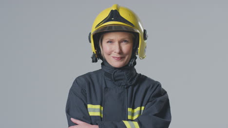 Studio-Portrait-Of-Smiling-Mature-Female-Firefighter-Wearing-Helmet-Against-Plain-Background