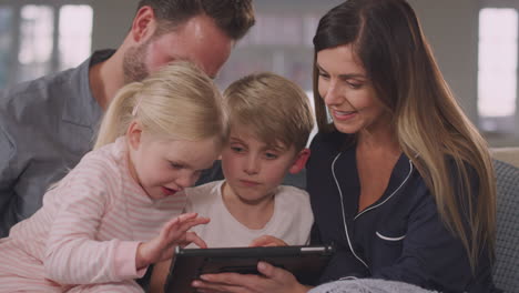 Lächelnde-Familie-Im-Schlafanzug,-Die-Auf-Dem-Sofa-Sitzt-Und-Spaß-Daran-Hat,-Gemeinsam-Ein-Digitales-Tablet-Zu-Nutzen