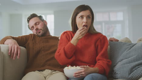 Man-Falls-Asleep-As-Couple-Sit-On-Sofa-With-Popcorn-Watching-TV