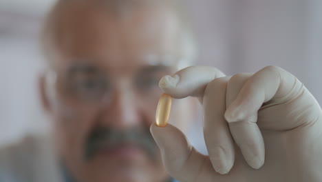 An-elderly-male-drug-developer-in-a-formalistic-company-picks-up-a-pill-in-his-hand-and-looks-at-it.-Medications-for-coronavirus.-High-quality-4k-footage