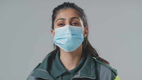 Studio-Portrait-Of-Young-Female-Paramedic-Wearing-Mask-Against-Plain-Background
