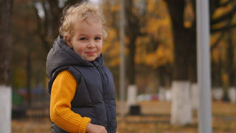cute-little-child-with-blonde-curly-hair-in-autumn-park-area-medium-portrait-of-funny-smiling-boy-happy-childhood
