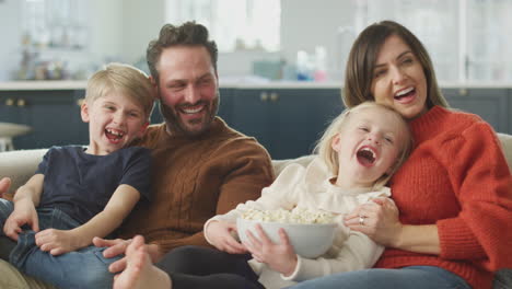 Familie-Sitzt-Mit-Popcorn-Auf-Dem-Sofa-Und-Schaut-Sich-Gemeinsam-Comedy-Im-Fernsehen-An