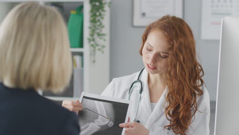Female-Doctor-Or-Consultant-Wearing-White-Coat-Having-Meeting-With-Female-Patient-To-Discuss-Scans