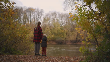 calm-weekend-trip-at-nature-little-boy-with-her-mother-are-standing-in-forest-and-looking-on-lake-enjoying-landscape-at-autumn-day-family-entertainment-together