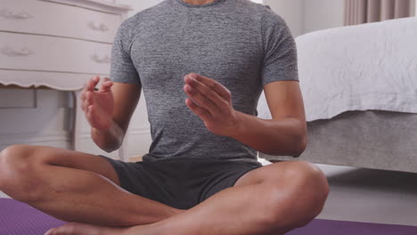 Close-up-dolly-shot-of-man-sitting-on-yoga-mat-in-bedroom-at-home-joining-hands-together---shot-in-slow-motion