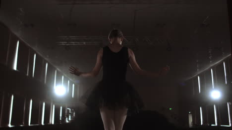 Close-up-of-ballet-dancer-as-she-practices-exercises-on-dark-stage-or-studio.-Ballerina-shows-classic-ballet-pas.-Slow-motion.-Flare-gimbal-shot.
