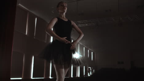 Graceful-woman-ballerina-in-a-dark-dress-on-a-dark-stage-of-the-theater-in-the-smoke-performs-dance-moves-in-slow-motion.