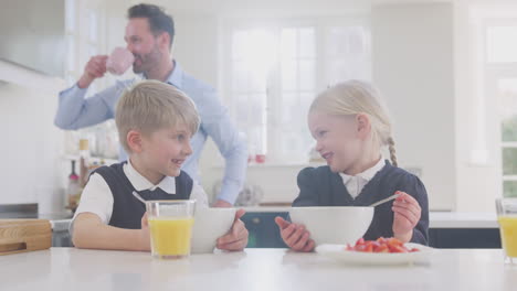 Zwei-Kinder-In-Schuluniform-Frühstücken-In-Der-Küche,-Während-Sich-Der-Vater-Für-Die-Arbeit-Fertig-Macht