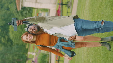 Vertical-Video-Of-Young-Couple-Travelling-Through-City-Together-Vlogging-To-Video-Camera-In-Park