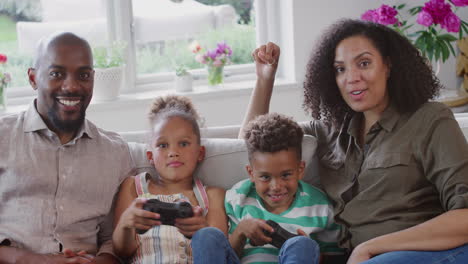 Eltern-Sitzen-Mit-Kindern-Zu-Hause-Auf-Dem-Sofa-Und-Spielen-Gemeinsam-Videospiele