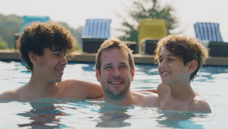 Portrait-Of-Father-With-Sons-Having-Fun-In-Outdoor-Swimming-Pool-On-Summer-Vacation-Together