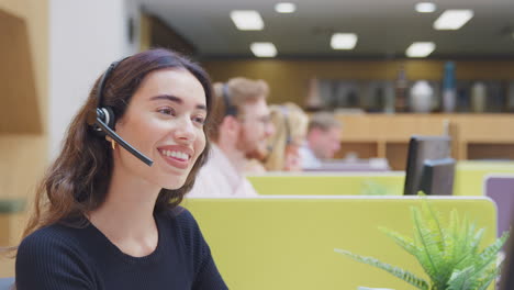 Businesswoman-Wearing-Phone-Headset-Talking-To-Caller-In-Customer-Services-Centre