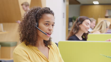 Portrait-Of-Businesswoman-Wearing-Phone-Headset-Working-At-Computer-In-Customer-Services-Centre