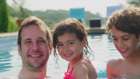 Portrait-Of-Multi-Racial-Family-Relaxing-In-Swimming-Pool-On-Summer-Vacation-Together