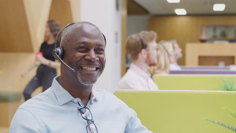 Portrait-Of-Mature-Businessman-Wearing-Headset-Talking-To-Caller-In-Customer-Services-Centre