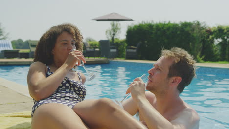 Couple-Relaxing-In-Swimming-Pool-On-Summer-Vacation-Celebrating-Drinking-Champagne