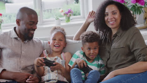 Parents-Sitting-On-Sofa-With-Children-At-Home-Playing-Video-Game-Together