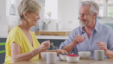 Retired-Couple-Sitting-Around-Table-At-Home-Having-Healthy-Breakfast-With-Fresh-Fruit--Together