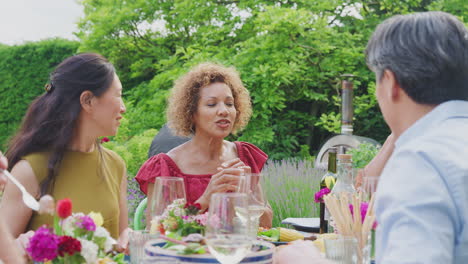 Group-Of-Mature-Friends-Talking-Around-Table-At-Summer-Dinner-Party-In-Garden-At-Home